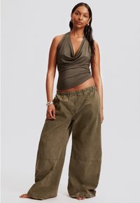 Top halter neck vert olive avec un tissu drapé, associé à un pantalon large à jambe large vert olive ample. Les deux présentent une texture douce et un design décontracté.