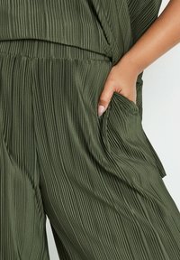 Olivgrön plisserad tygoutfit med en avslappnad passform, som har en sidficka och en mjuk textur.
