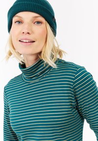 Teal coltrui met dunne gouden strepen, voorzien van een geribde kraag, zachte textuur en lange mouwen, gestyled met een bijpassende beanie.