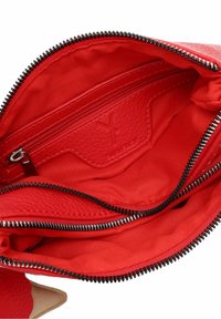 Rød læder håndtaske indvendigt med en lynlås lomme og stofforing. Detaljer inkluderer sorte lynlås tænder og en struktureret læder kortlomme.
