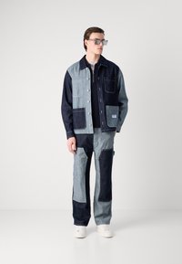 Denim jacket and pants set featuring patchwork design in light and dark blue tones, with multiple pockets and light texture.