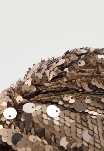 Pyöreä koriste-esine, joka on päällystetty päällekkäisillä pronssisilla paljeteilla, ja siinä on sileä pinta, kiiltävät yksityiskohdat sekä pienet kiinnitysreiät.