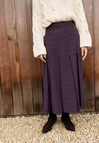 Dolga, nabrana krilo v mornarsko modri in bordo kockasti vzorec, izdelano iz mehke tkanine. Kombinirano s temno rjavimi gležnjarji s koničastimi konicami.