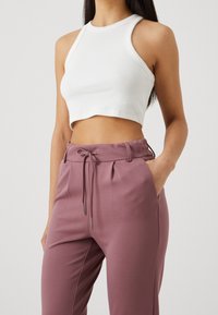 Vit ribbad crop top med hög halsringning, tillsammans med ljuslila byxor med elastisk midja och dragsko med metallaglar.