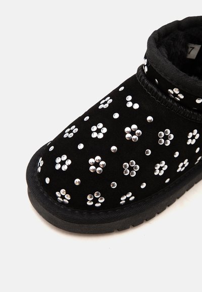 Μαύρο παπούτσι τύπου slip-on με ασημένιες στρογγυλές τρουκς διατεταγμένες σε λουλουδάτα σχέδια και μαλακή, υφασμάτινη εσωτερική επένδυση.