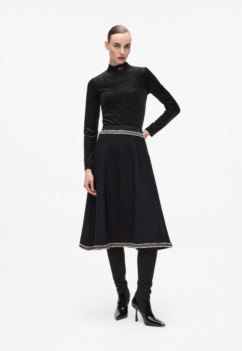 Black long-sleeve top with a shimmery texture and a high neck, paired with a knee-length black skirt featuring a silver-accented hem.