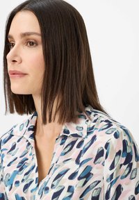 Hemdbluse aus einem leichten Stoff mit einem mehrfarbigen abstrakten Muster, das Designs in Blau, Rosa und Creme mit Pinselstrichen zeigt.
