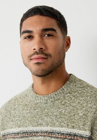 Pletený sveter v olivovo zelenej farbe s textúrovaným povrchom, s okrúhlym výstrihom a horizontálnymi pruhmi v šedej, bielej a oranžovej farbe.