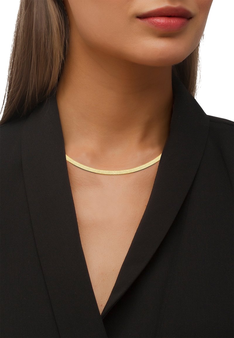 Femme portant un collier chaîne doré élégant avec un blazer noir, montrant le cou et le bas du visage sans yeux ni cheveux visibles.