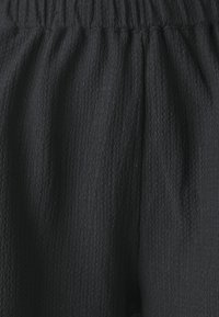Black textured fabric pants with a gathered waistband. The surface features a subtle, dimensional pattern, providing a soft appearance.