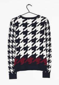 Maglione lavorato a maglia con un motivo a scacchi houndstooth in blu navy e bianco, con un accento bordeaux all'orlo. Maniche lunghe, design con scollo rotondo.