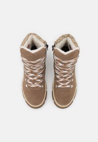 Bottes de randonnée en suédé marron avec des lacets tressés blancs et dorés, doublure blanche en peluche et semelle extérieure texturée beige. Comprend un col rembourré.