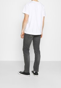 Camiseta blanca de algodón combinada con jeans oscuros ajustados y zapatillas de lona negras. Los jeans presentan un diseño típico de cinco bolsillos.