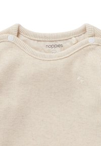 Cremefarvet, ribbet babydragt med rund hals, trykknapper og en lille broderet blomstebeskrivelse på brystet.