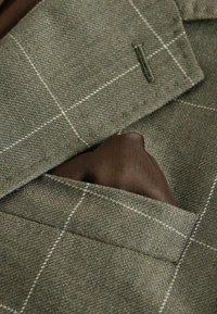 Poche d'une veste à carreaux verts avec un carré de soie brun foncé soigneusement plié à l'intérieur.