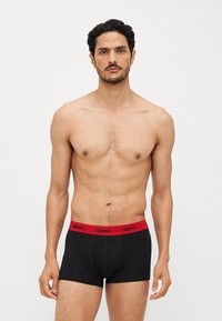 Schwarze Boxer-Shorts mit rohem elastischem Taillenband, das das „DIESEL“-Logo zeigt. Der Stoff wirkt glatt und eng anliegend, mit einer klassischen Trunk-Form.