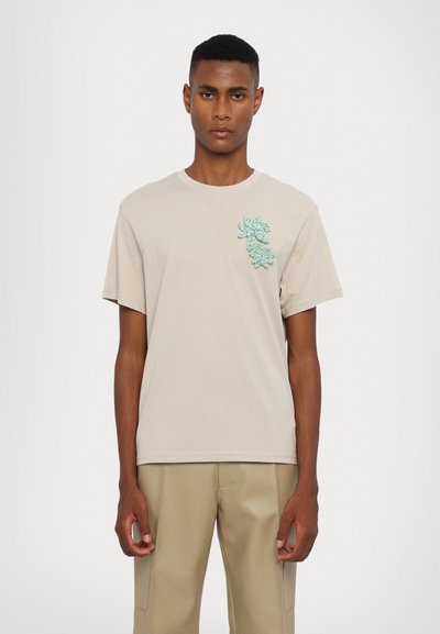 Light beige cotton t-shirt featuring an aqua green embroidered floral design on the left chest area. Short sleeves and a crew neck.