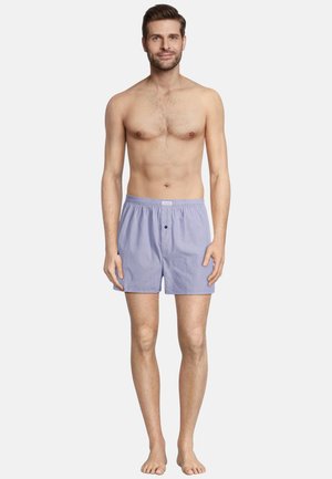 Helle lila Baumwollboxershorts mit einem dezenten Streifenmuster, elastischem Bund und einem einzigen Knopfverschluss, getragen von einem barfüßigen Mann.