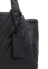 Svart kviltad handväska i konstläder med diagonala stygn och en rektangulär ALDO-märkesetikett fäst med kedja på handtaget.