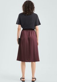 Bordowa spódnica z satyny z elastycznym paskiem w talii, o długości do połowy łydki, o gładkiej fakturze. Połączona z czarnym topem z krótkim rękawem i sandałami.
