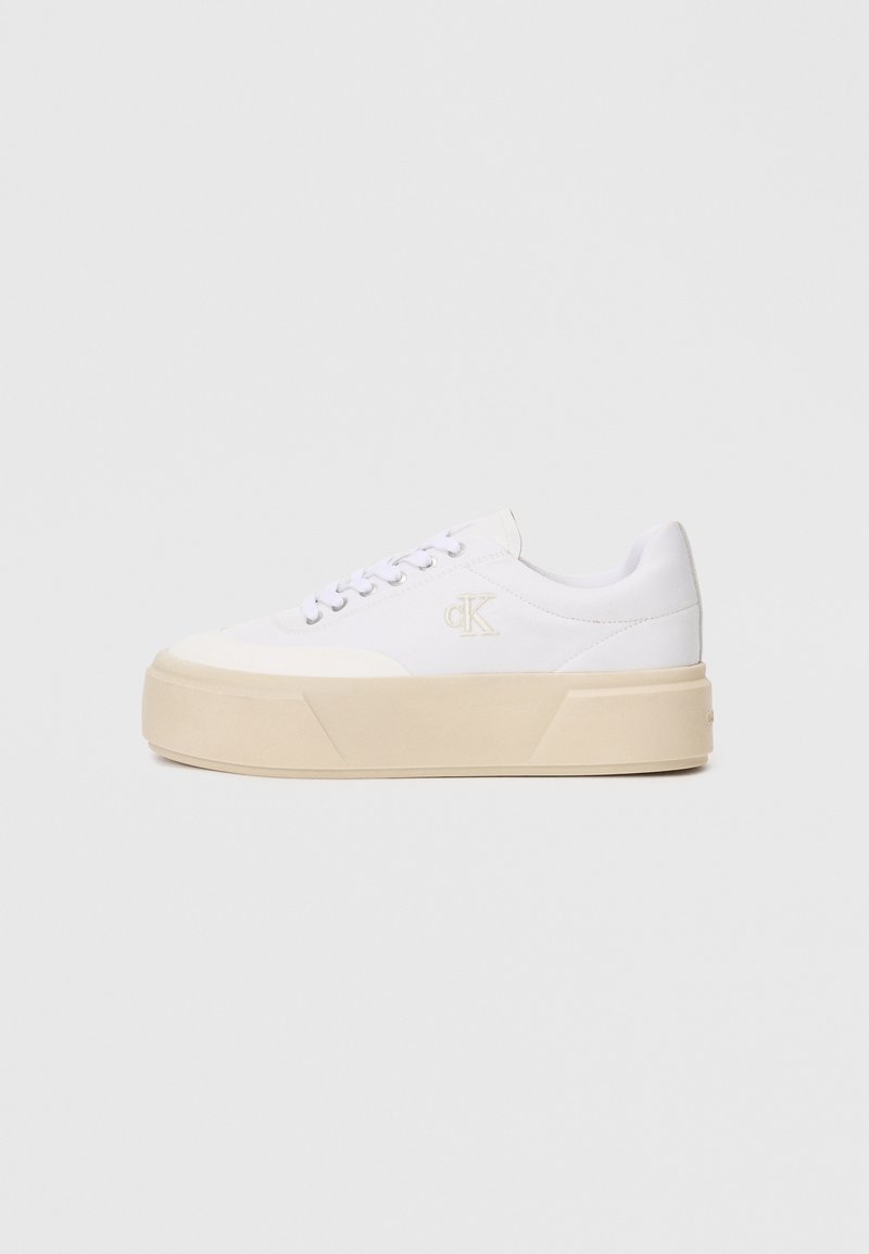 Λευκά πάνινα sneakers με πλατφόρμα, επίπεδες κορδόνια και μια διακριτική λογότυπο στο πλάι. Καθαρός σχεδιασμός με ομαλές υφές και ελάχιστες λεπτομέρειες.