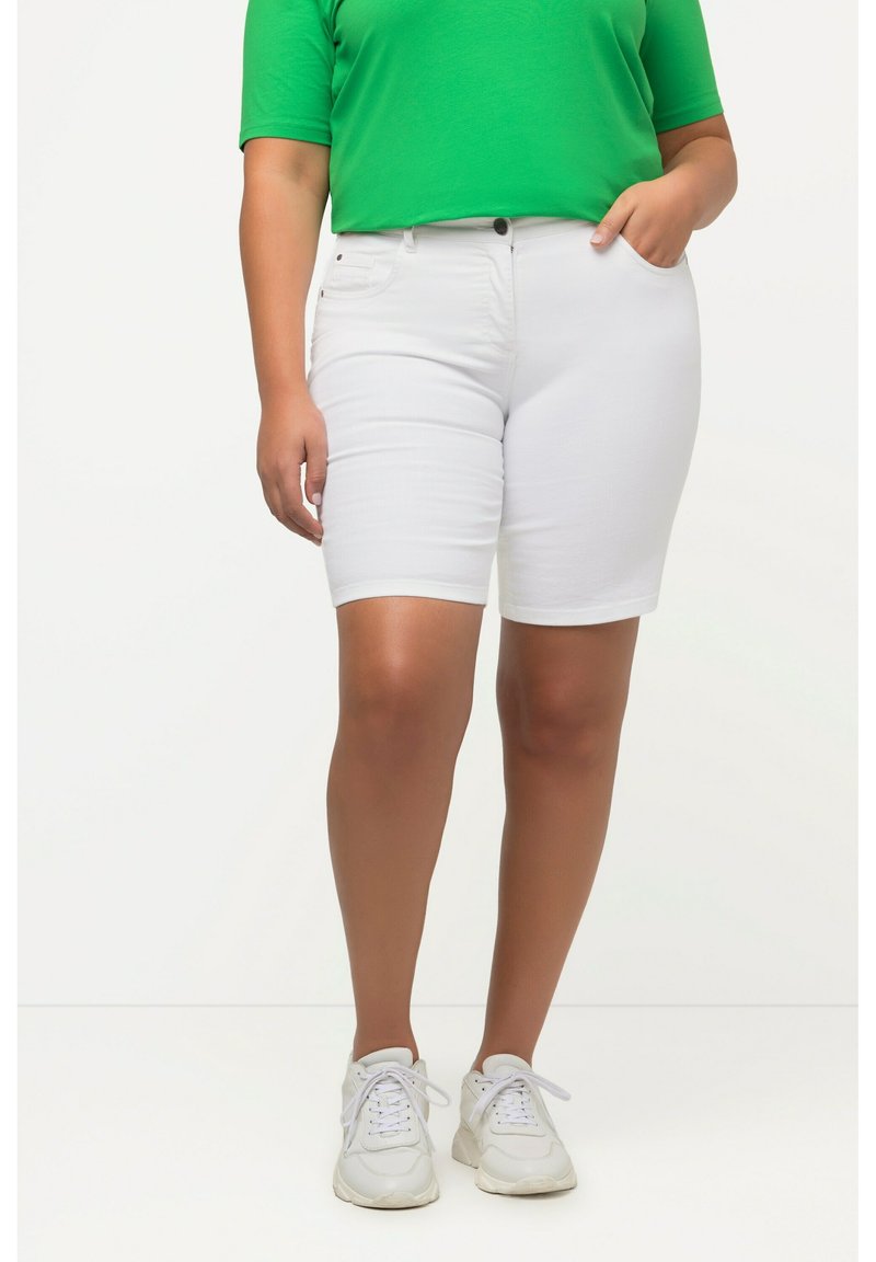 Pantalones cortos de denim blanco con un diseño ajustado, bolsillos laterales y cierre de botón. Combinados con una camisa verde de manga corta y zapatillas blancas.