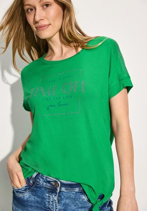 Grøn T-shirt med opfoldede ærmer, prydet med en grafisk print i rhinsten, der står "TAKE IT EASY TIME OFF." Blødt, afslappet stof, løs pasform.