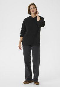 Schwarzer Strickpullover mit entspannter Passform und weitem Kragen, kombiniert mit dunkelgrauen geraden Jeans und braunen Plateauschuhen.