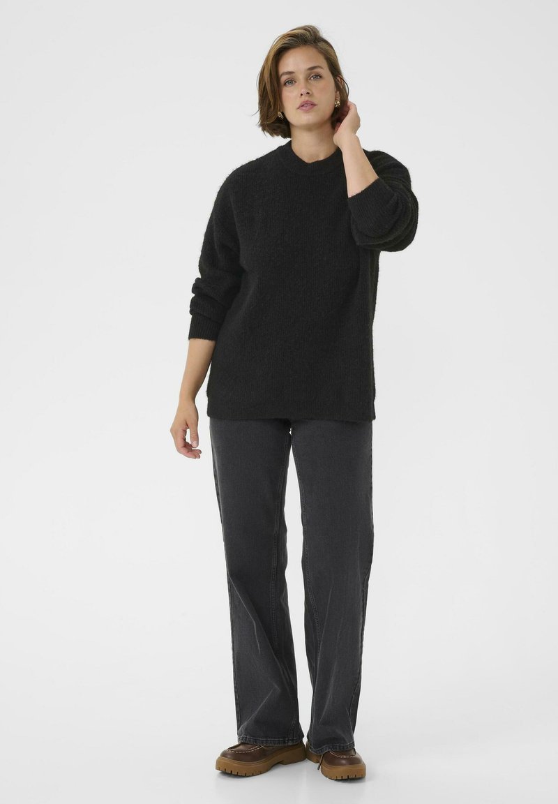 Schwarzer Strickpullover mit entspannter Passform und weitem Kragen, kombiniert mit dunkelgrauen geraden Jeans und braunen Plateauschuhen.