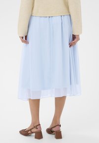 Světle modrá midi sukně s vrstveným designem a průsvitnou texturou, doplněná hnědými sandály na blokovém podpatku s tkaným vzorem.