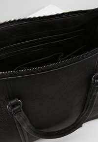 Zwarte leren handtas met een ritssluiting, interne compartimenten en stevige handvatten. Textuur oppervlak met zichtbare stiksels.