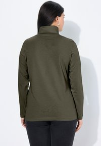 Khaki dlouhé tričko s rolákem s měkkou texturou a přiléhavým střihem, které zdůrazňuje vysoký límec a jemné detaily šití.