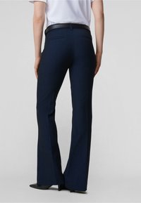 Tmavě modré rozšířené kalhoty z texturované látky, s hladkým černým pasem, dvěma zadními kapsami a krejčovsky upraveným střihem.
