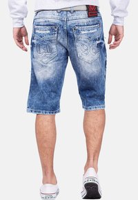 Shorts en denim bleu clair avec une finition décolorée. Présente des accents usés, des poches arrière brodées et une coupe régulière.