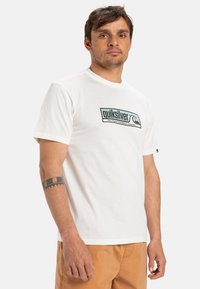 Bílý bavlněný tričko s obdélníkovým logem Quiksilver v zelené a modré barvě, umístěné na jednobarevném pozadí, krátké rukávy a kulatý výstřih.