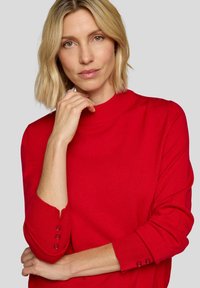 Roter Pullover mit hohem Kragen und dreiviertellangen Ärmeln. Strukturierter Strickstoff mit Knopfakzenten an den Ärmelabschlüssen. Glatte Oberfläche.