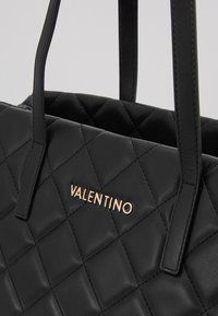 Juodas siuvinėtas odinis rankinės su auksiniu "VALENTINO" logotipu. Ypatybės: dvi juodos rankenos ir tekstūruotas paviršiaus raštas.