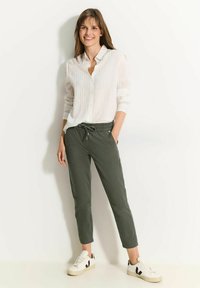 Witte, lange mouwen, blouse met verticale strepen; groene, te strikken, cropped broek; witte sneakers met zwarte accenten.