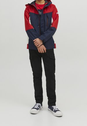 Marineblaue, rote und weiße Jacke mit einem Reißverschluss vorne, verstellbarem Kapuzenriegel und zwei Seitentaschen. Kombiniert mit schwarzen Cargo-Hosen und Sneakers.