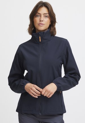 Veste softshell bleu marine avec un col haut, fermeture éclair, poignets élastiques et poches latérales. Présente un design minimaliste et une texture lisse.