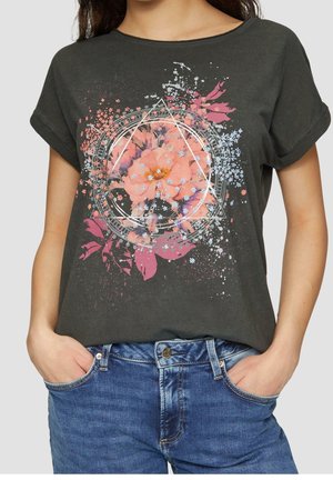 T-shirt gris foncé à manches retroussées avec imprimé floral rose et violet et formes géométriques porté avec un jean bleu, mains dans les poches.