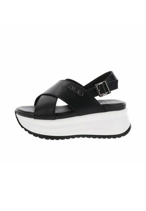 Sandale plateforme en cuir noir avec semelle épaisse blanche, brides croisées, boucle de cheville réglable et logo "4US" sur la bride latérale.