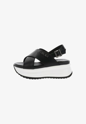Sandalia de plataforma de cuero negro con suela blanca gruesa, tiras cruzadas, hebilla ajustable en el tobillo y logo "4US" en la tira lateral.