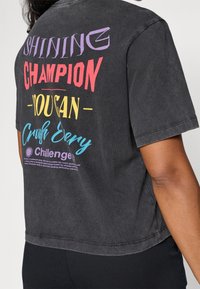 Grå bomulds oversized t-shirt med multikolor tekst på ryggen: "SKINNENDE MESTER DU KAN Knuse Hver Udfordring" med logo detalje.