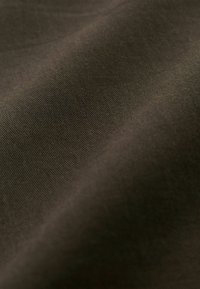 Mīksts, tumši zaļš audums ar gludu tekstūru un smalku rievotu rakstu, kas parāda nelielas krāsu un spīduma nianses.