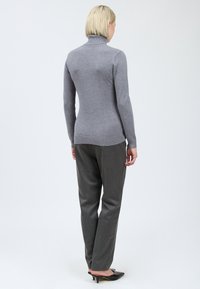 Pull à col roulé gris avec des manches longues, corps cintré et ourlet côtelé, associé à un pantalon gris et des chaussures à talons noires. Fond uni.
