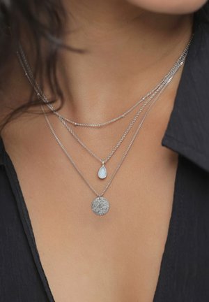 Geschichtete Silberketten mit einem strukturierten, runden Anhänger, einem tropfenförmigen Edelstein und feinen Ketten mit kleinen Perlenakzenten.