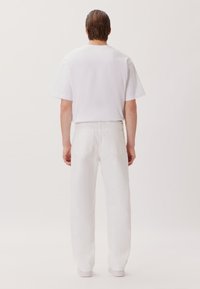 T-shirt bianco a girocollo abbinato a jeans bianchi a gamba dritta. Il materiale sembra cotone; la vestibilità è rilassata con una superficie liscia.