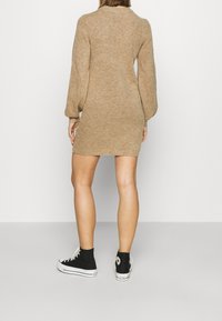 Ruskea neulemekko, jossa on pitkät pullistuvat hihat, kylkeen istuva muoto ja ribbireuna, yhdistettynä mustiin kangaskorkeisiin lenkkareihin.