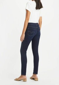 Slim-fit mörkblå jeans i denim med klassisk femficksdesign, gul sömnad och logotyp på de bakre fickorna.